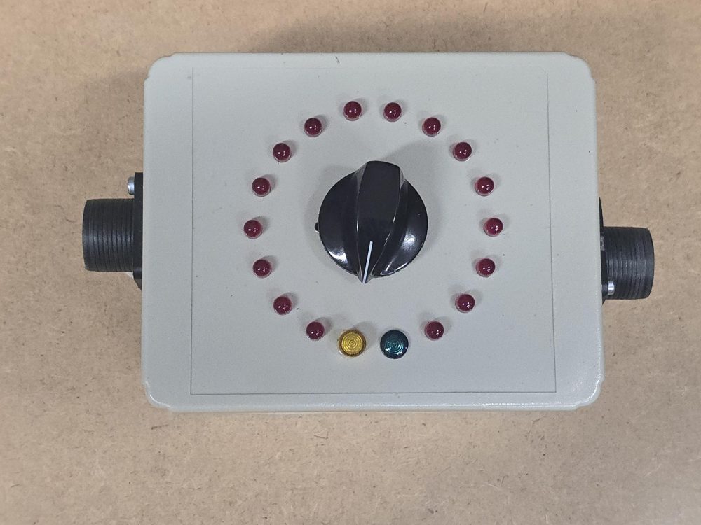 Grey cable checker with a ring of sixteen red indicator lights around a rotary knob and a connector on each side
