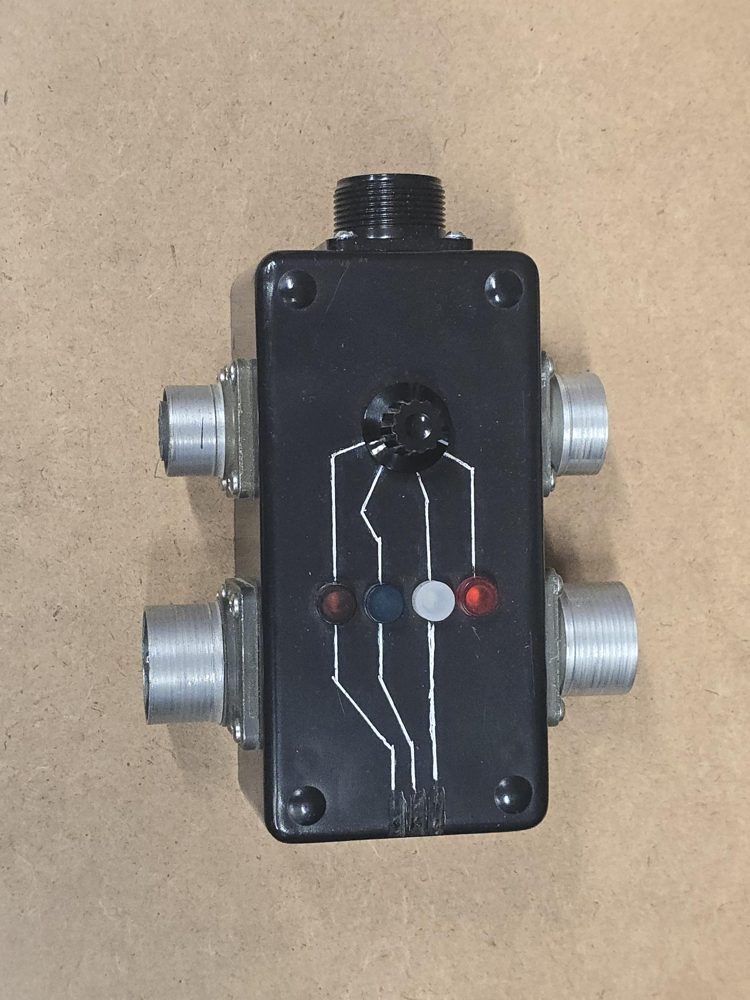 Black cable checker with four indicator lights, a selector knob, and five round connectors