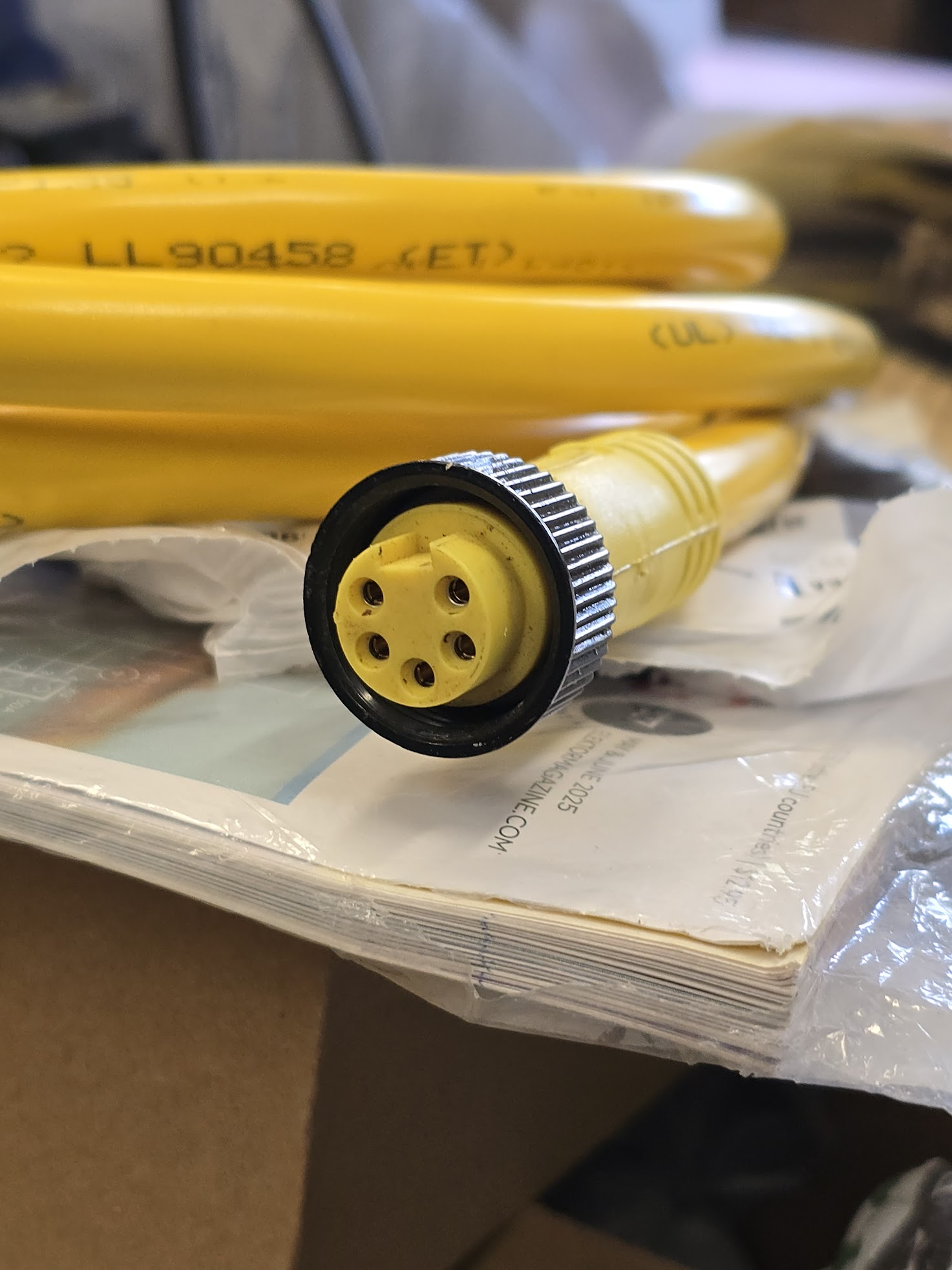 Close-up of a yellow industrial electrical connector surrounded by coiled cables and paperwork, highlighting its importance for safe equipment connections.