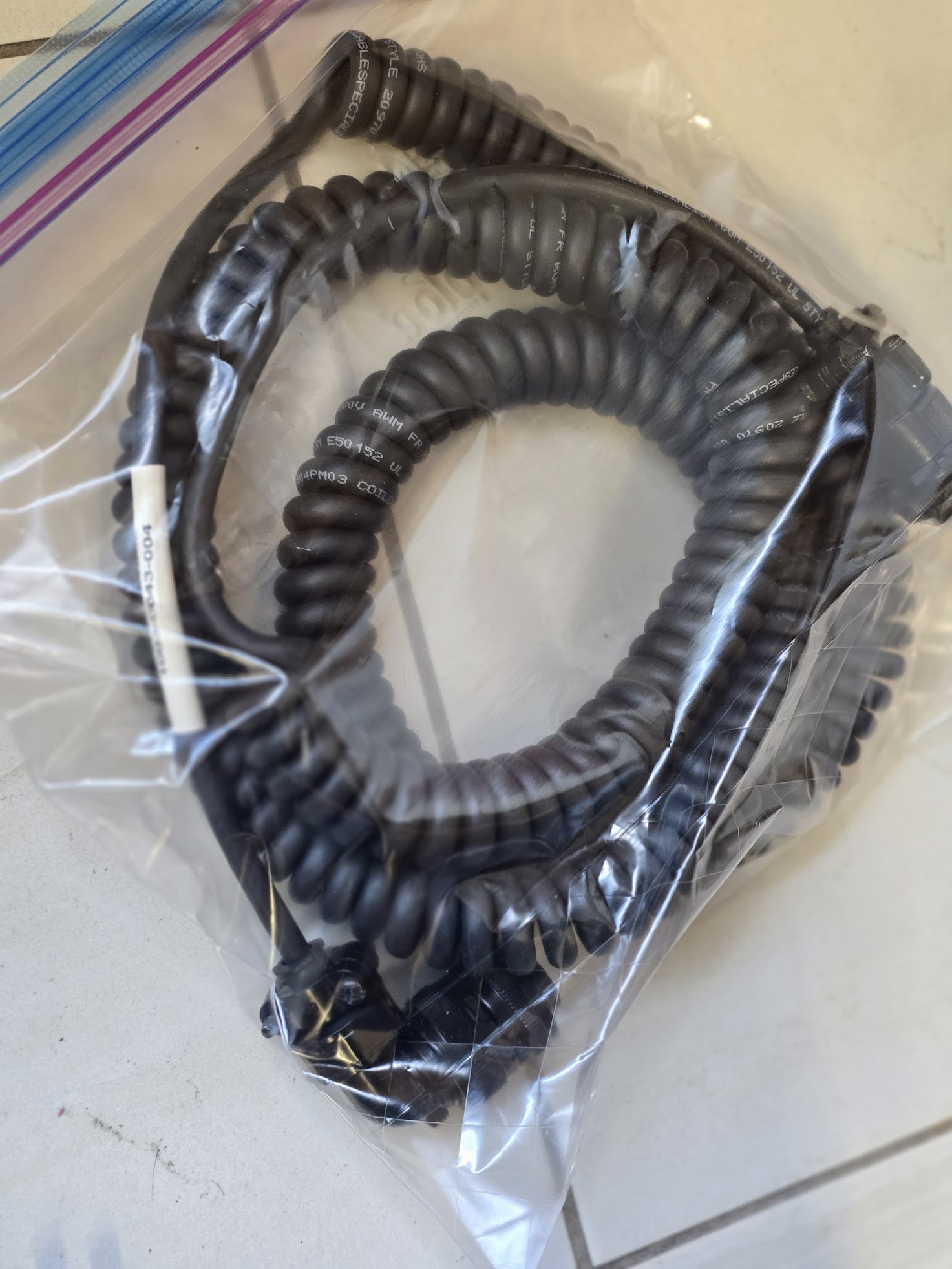 Coiled black cable inside a clear plastic ziplock bag, likely used for audio or telecommunications equipment.